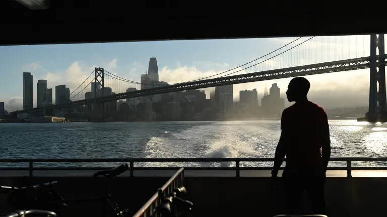 Silhouette of a person riding a ferry boat on the San Francisco Bay, looking at the San Francisco skyline and San Francisco-Oakland Bay Bridge.