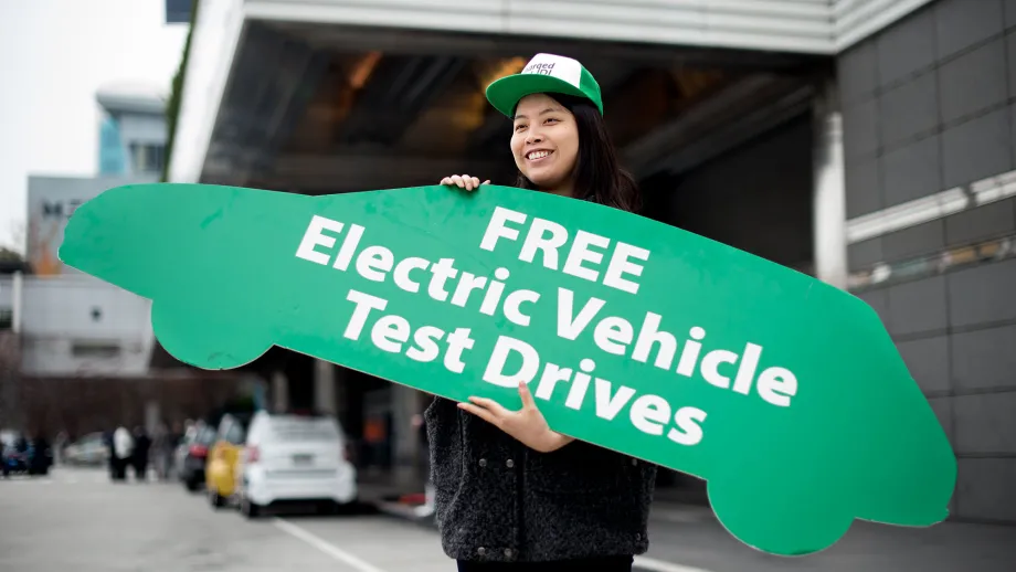 Woman holding a sign that says free electric vehicle test drives