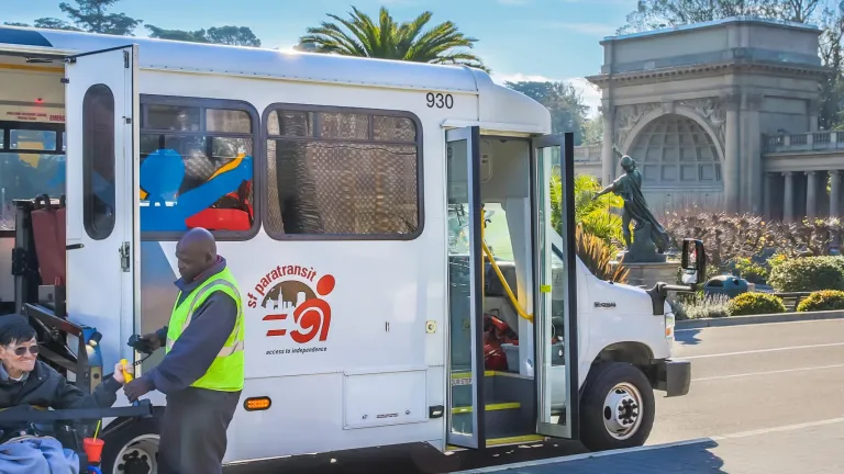 A person using a wheelchair is assisted in using the vehicle lift on an SF Paratransit bus