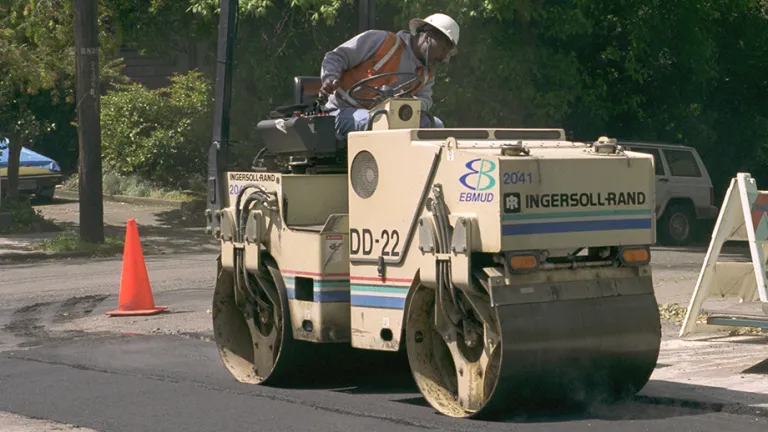 A road repair person driving a road roller over fresh pavement.