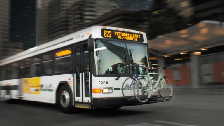 An AC Transit All-Nighter bus with two bicycles loaded into the front rack.