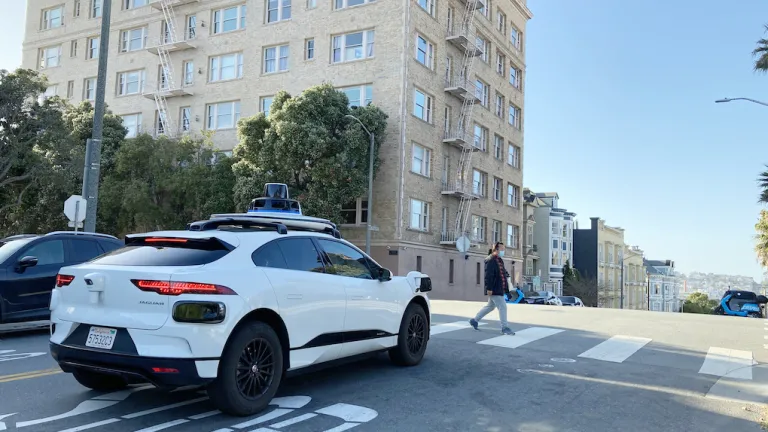  An automated vehicle waits while a person crosses at a crosswalk.