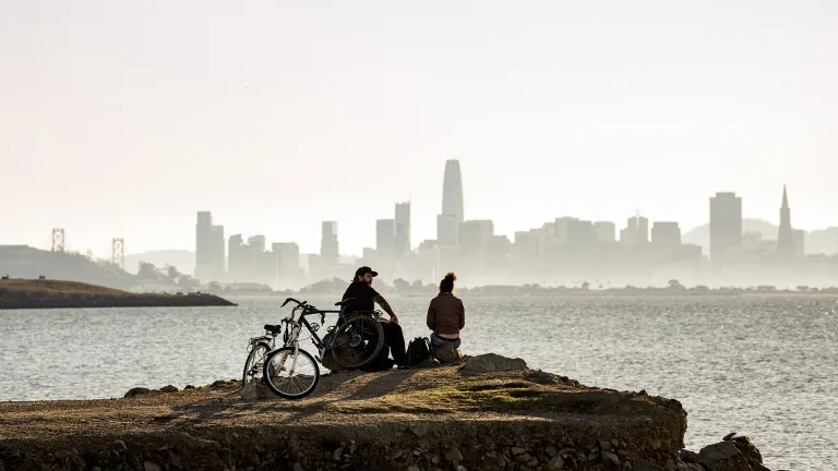 Two people at a Treasure Island waterfront park look at the San Francisco skyline.
