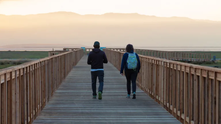 Two people walking along a Bay Trail boardwalk at sunset.