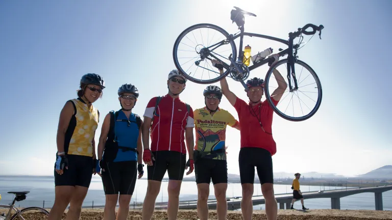A group of smiling adult cyclists, one holding a bicycle above his head, at the opening of the Benicia-Martinez Bridge bicycle-pedestrian path.