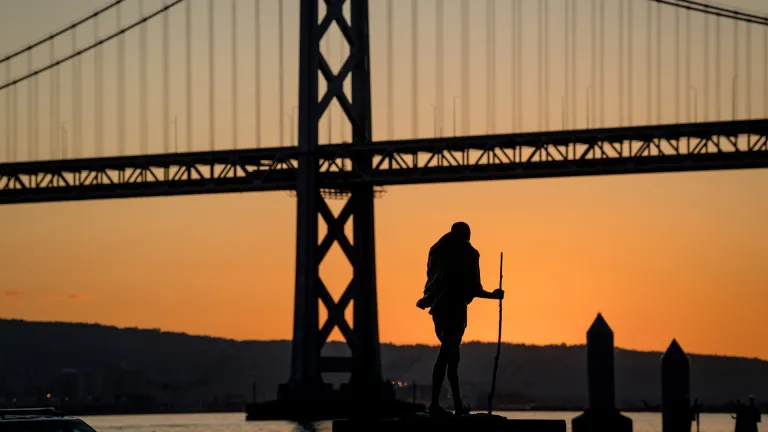 Silhouette of a Ghandi statue at San Francisco’s Ferry Building at dawn, with the San Francisco-Oakland Bay Bridge in the background.
