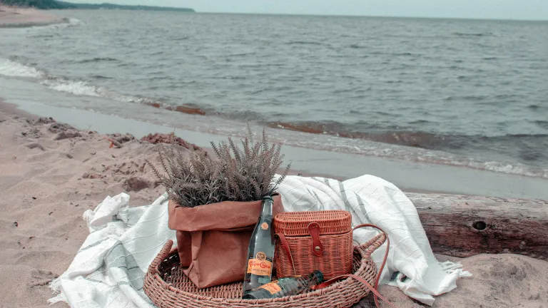 A picnic basket and blanket on the sand at a beach.