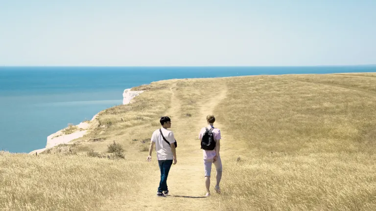 Two people hiking on a grassy cliff by the water.