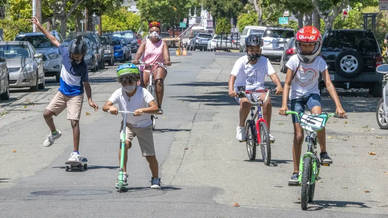A group of kids riding bikes, scooters and skateboards.