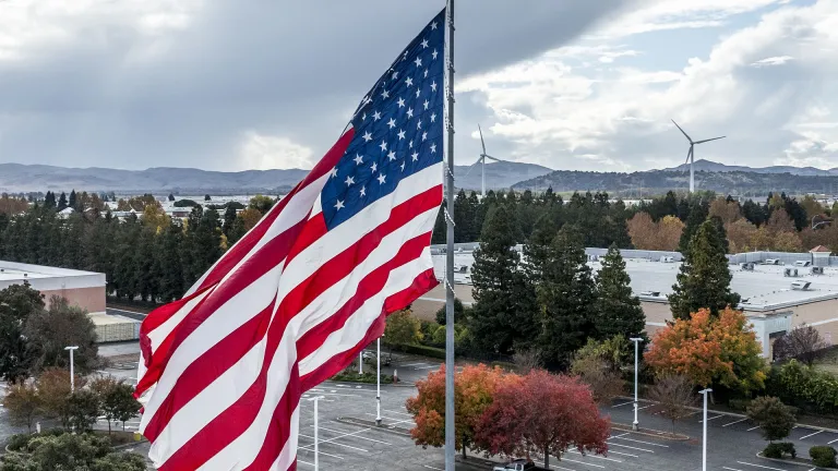 An American Flag blowing in the breeze, with industrial windmills in the background.