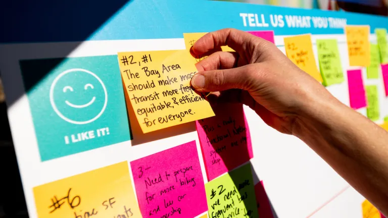 At a public engagement event, a person places a sticky note with their ideas on a board.