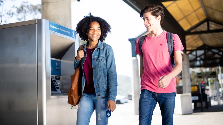 Two smiling people walking through a transit station.