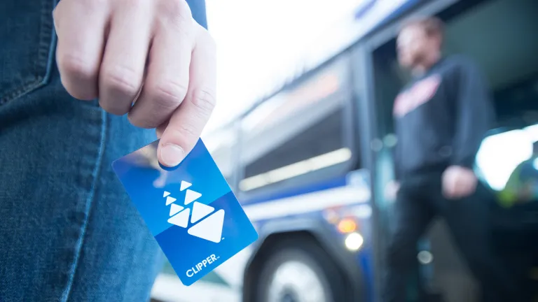 Closeup of a person holding a Clipper card as they wait to board a bus.