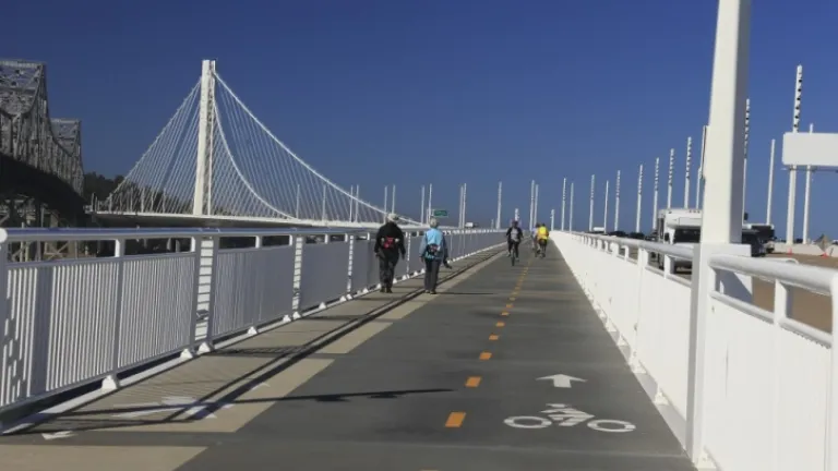 Pedestrians and cyclists use the East Span bicycle and pedestrian path, traveling westward with the self-anchored suspension tower int he background.