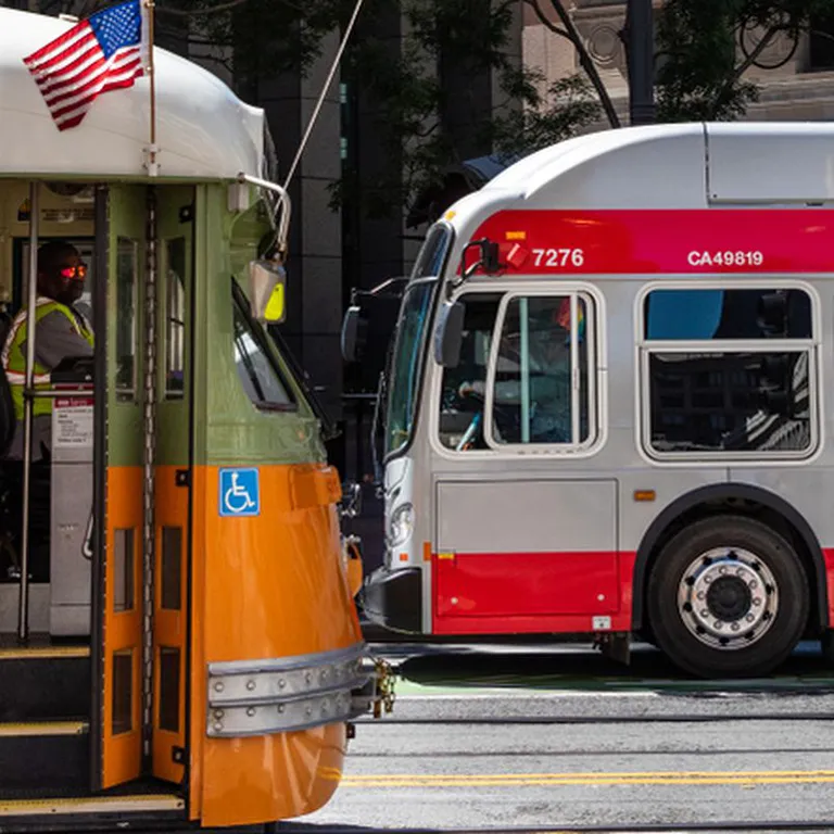 A Muni historic streetcar and modern bus pass each other in San Francisco.