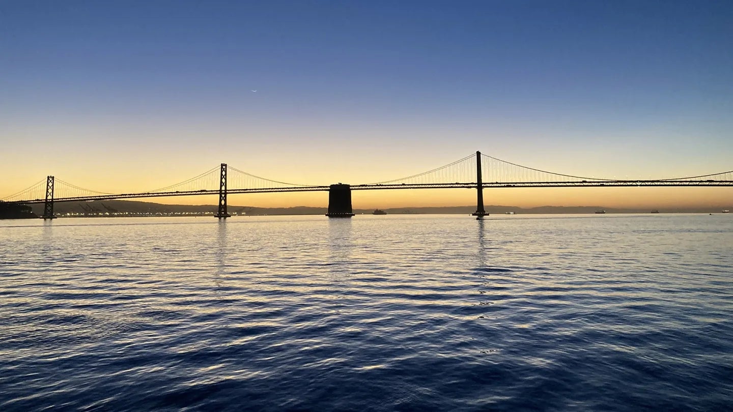 The sun rising behind a silhouette of the San Francisco-Oakland Bay Bridge.