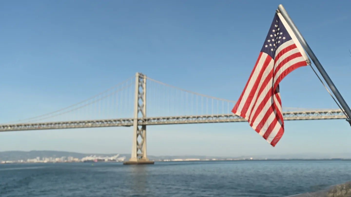 An American flag in front of the San Francisco-Oakland Bay Bridge.