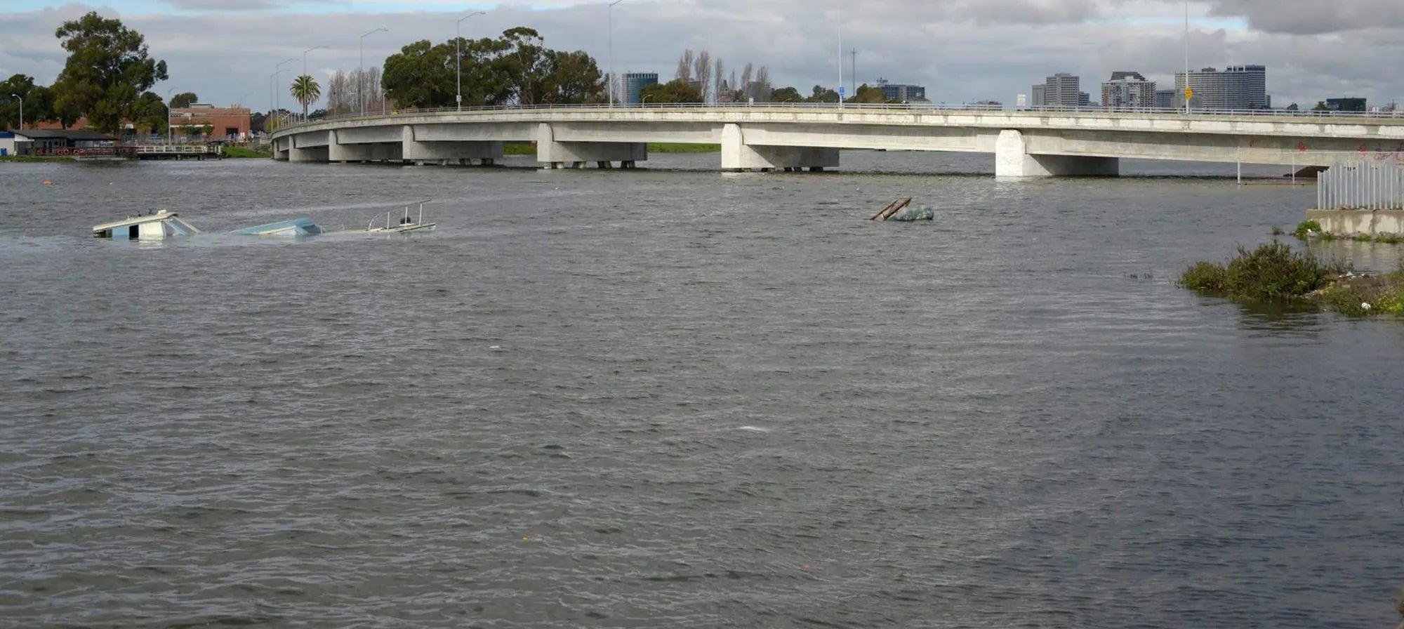 King tide at Coast Guard Island in Oakland. A boat sits sinking below the water, and the water level reaches nearly the underside of the bridge.