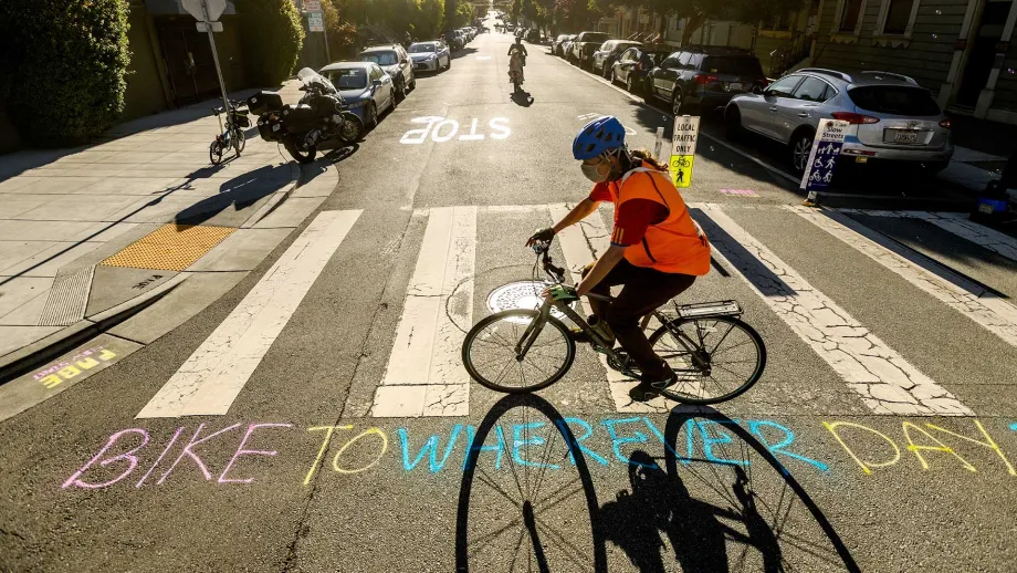 A cyclist rides past a crosswalk with Bike to Wherever Day written in chalk on the street.