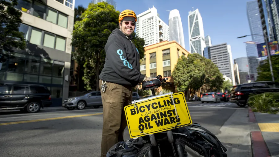 A cyclist with a "bicycling against oil wars" sign on Bike to Wherever Days 2025.