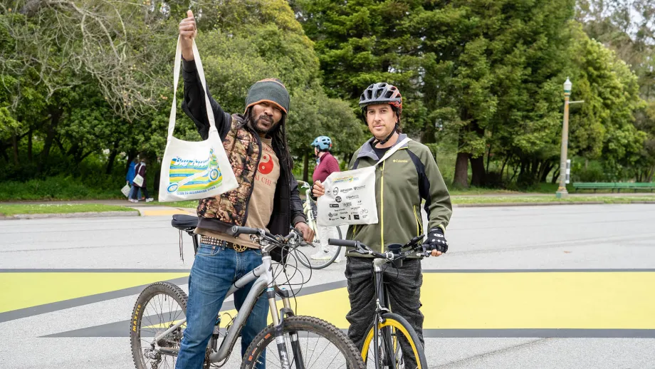 Two cyclists happily hold their Bike to Work Day tote bags.