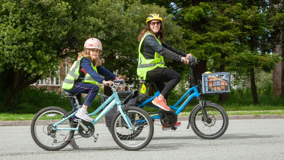 An adult and child riding bikes in neon safety vests in Golden Gate Park.