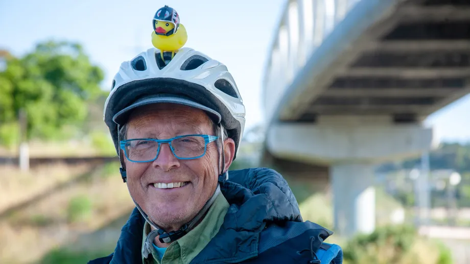 A smiling cyclist is wearing a helmet with a rubber duckie attached to the top.