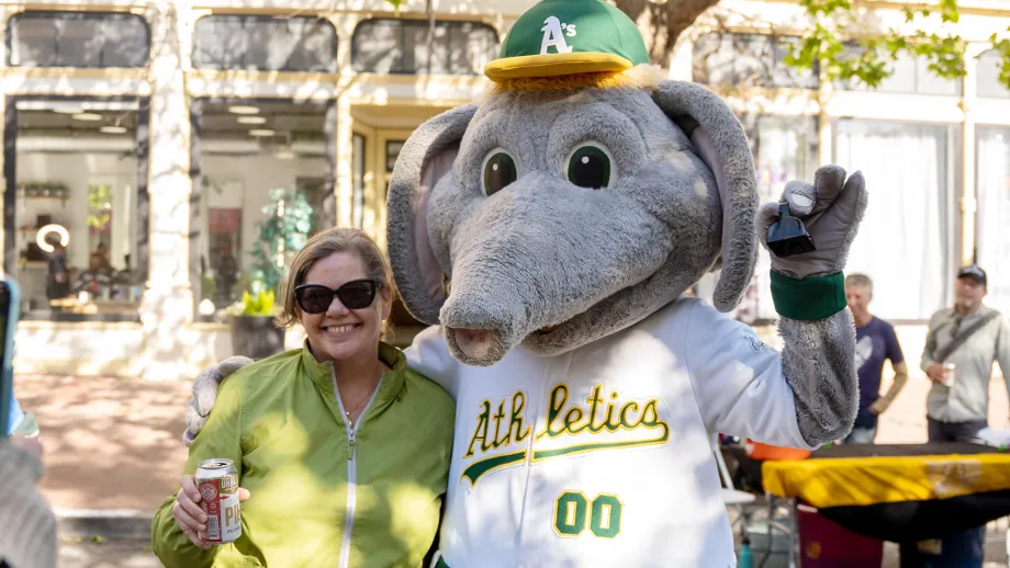 A woman in a green jacket poses with Stomper, the Oakland A's baseball elephant mascot.