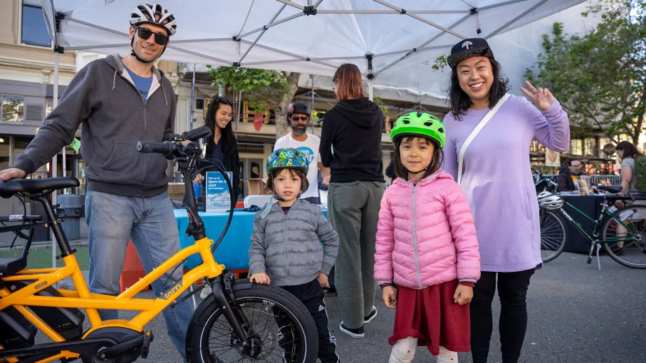 Two adults and two children pose for a photo with a yellow bicycle on Bike to Work Day.