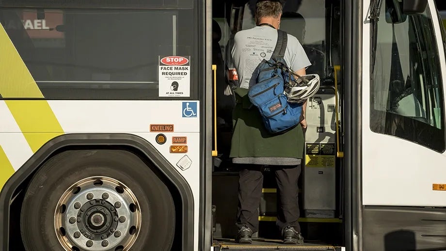 Man with a bicycle helmet is boarding a Golden Gate Transit bus.