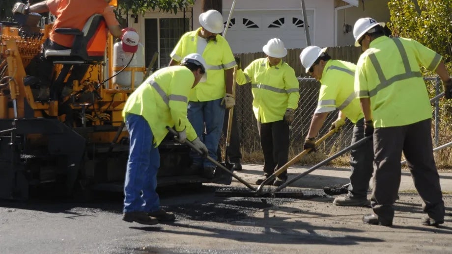 A six-person road crew performing pavement maintenance.