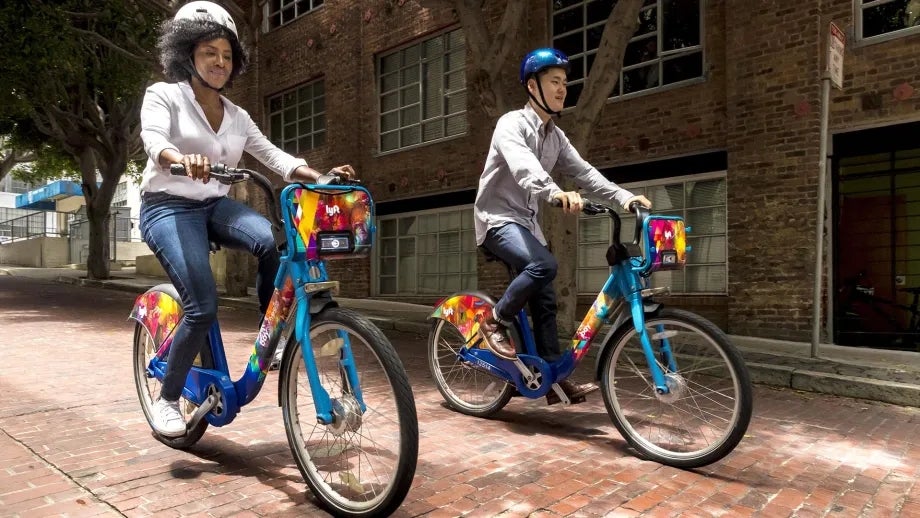 Two adults, each riding a Bay Wheels bike share bicycle.