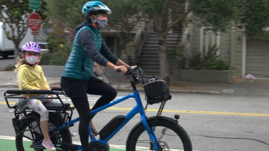 An adult and young child ride an electric-assist bicycle in a green-painted bikeway.