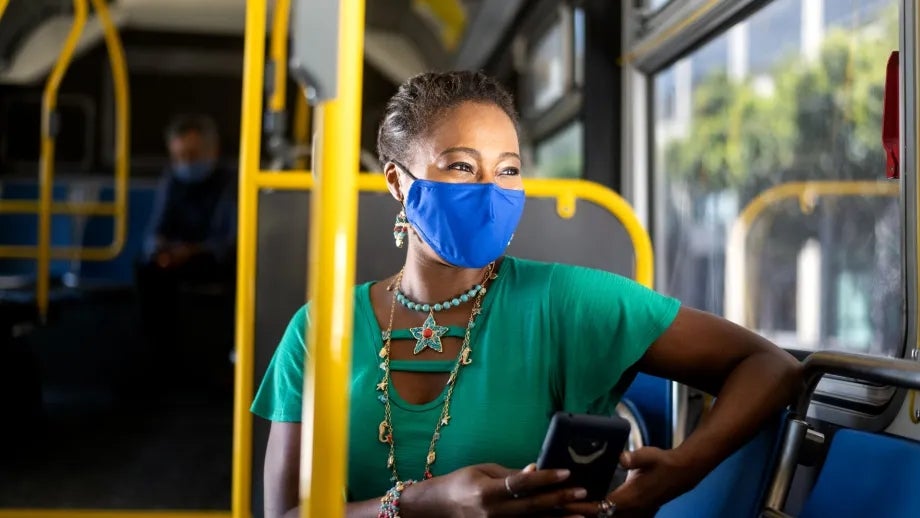 A woman wearing a mask looks out the window while seated on a bus.