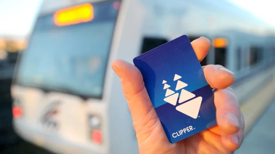 A person's hand holding a Clipper card, in front of a VTA light rail train.
