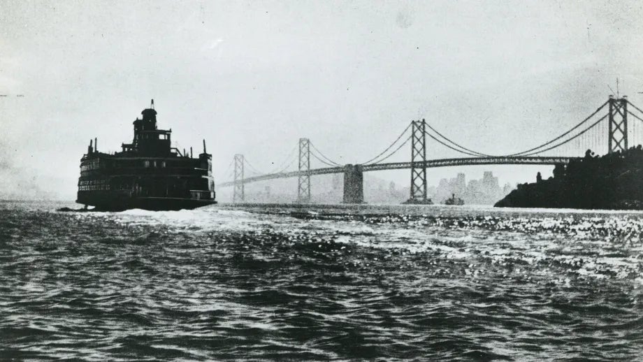 Historic photo of a steam-powered ferry boat traveling on the bay near the San Francisco-Oakland Bay Bridge, shortly after the bridge opening.