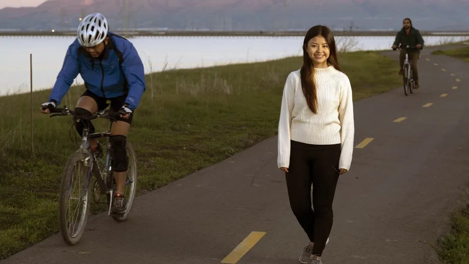 A woman walks on a mixed-use path on the Bay Trail as cyclists ride by.
