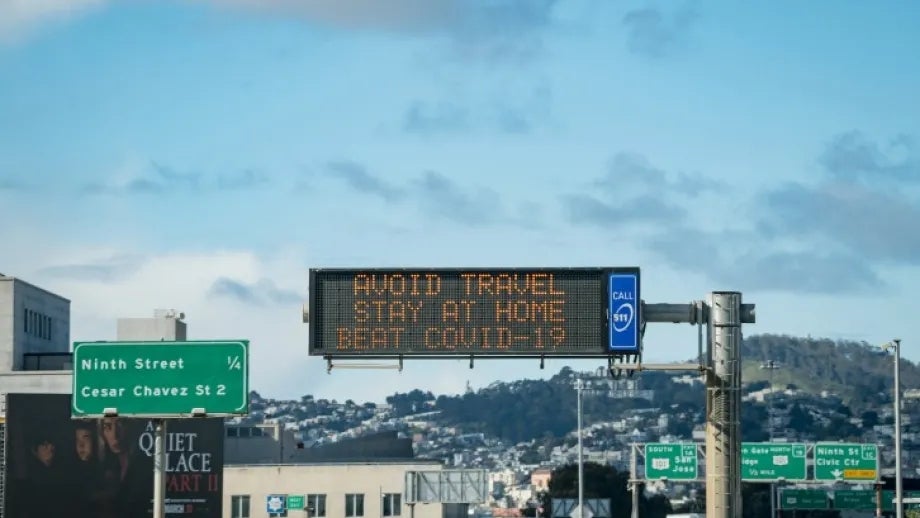 Motorists travel on southbound U.S. 101 in San Francisco, with a sign for Ninth Street and Cesar Chavez Street on the left and a changeable message sign in the center that reads "Avoid travel stay at home beat COVID-19"