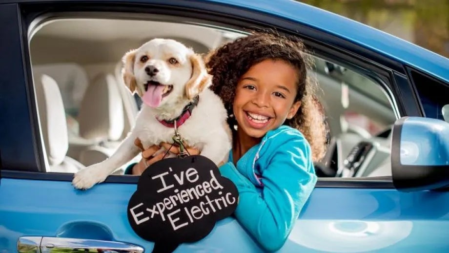 A girl and dog sit in an electric vehicle at an "Experience Electric" event San Jose.