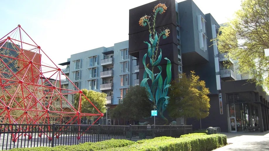 A beautiful flower mural on the side of a tall affordable housing complex in San Jose, with a playground in the foreground.