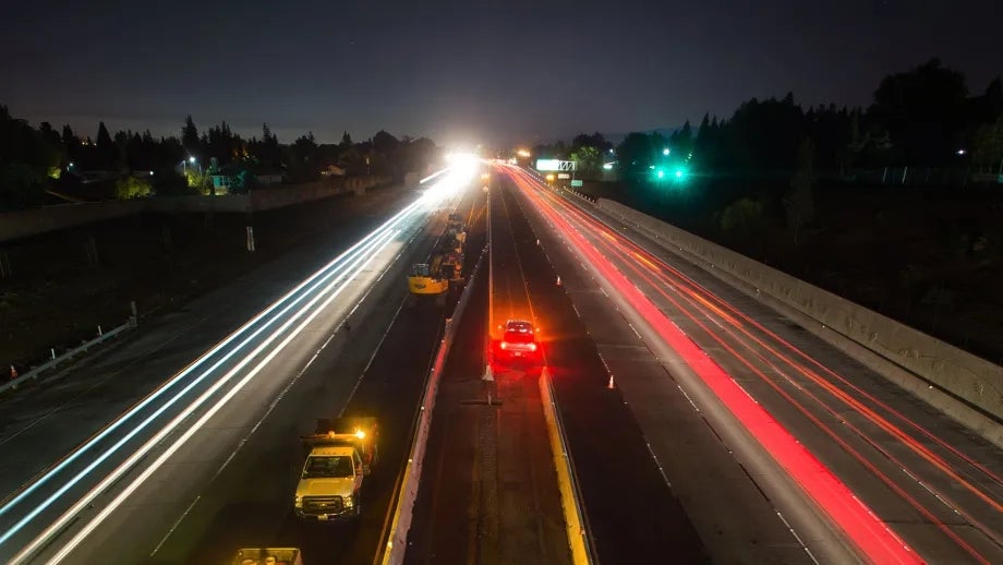 A long-exposure photo shows cars streaking down the highway at night.