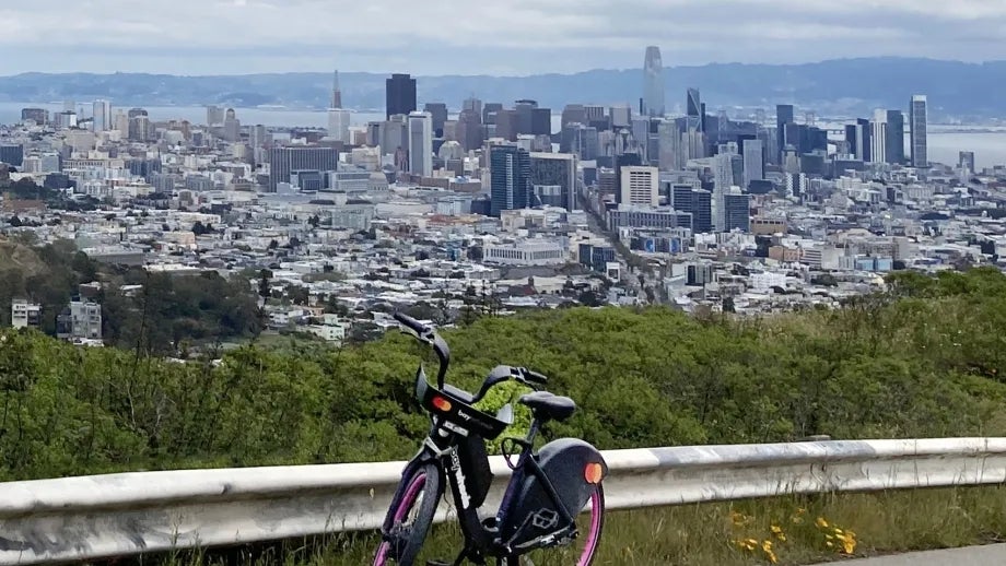 A Bay Wheels bikeshare e-bike on Twin Peaks, with a view of downtown San Francisco in the background.