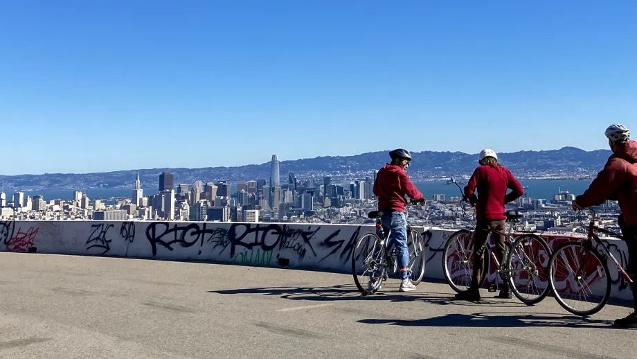 Three cyclists on Twin Peaks look down on downtown San Francisco.