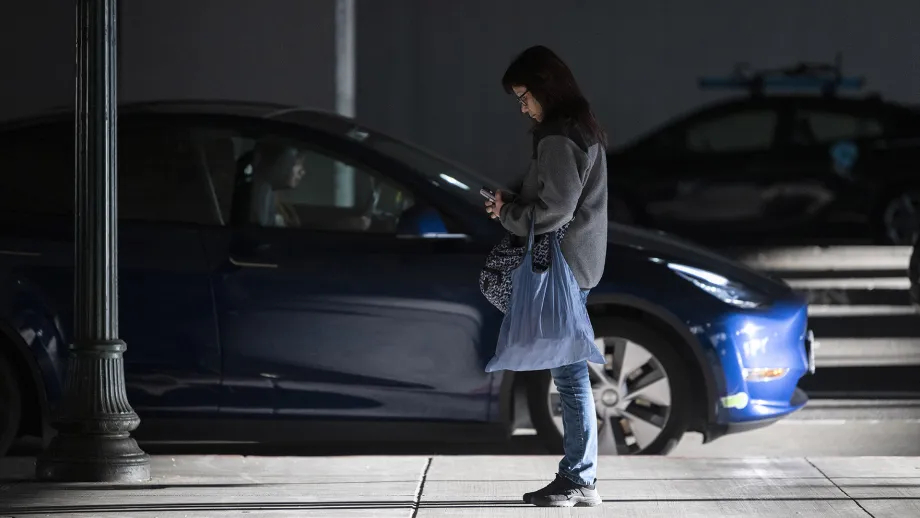 A woman looking at her phone next to a vehicle passenger pickup area at MacArthur BART station.