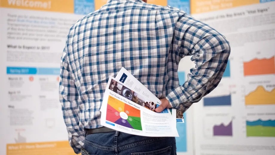 A man with his back to the viewer holds informational sheets behind his back while standing in front of display boards at the Plan Bay Area 2040 open house in Napa.