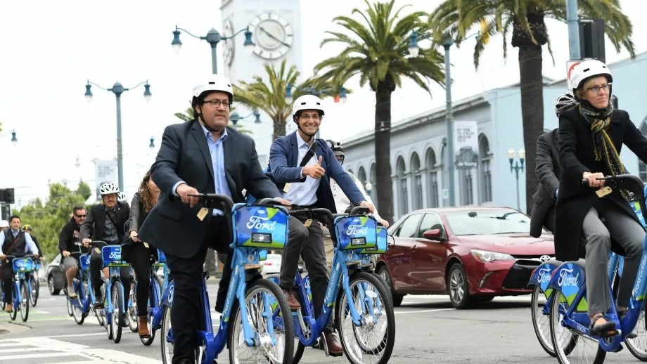 Individuals riding Ford GoBikes in front of the San Francisco Ferry Building.