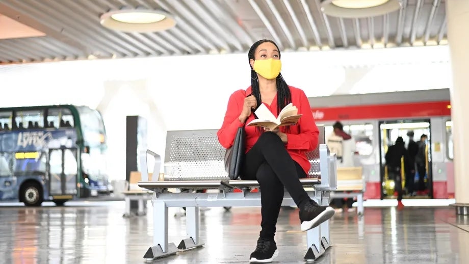 A masked woman reads a book while waiting for her bus at the Salesforce Transit Center.