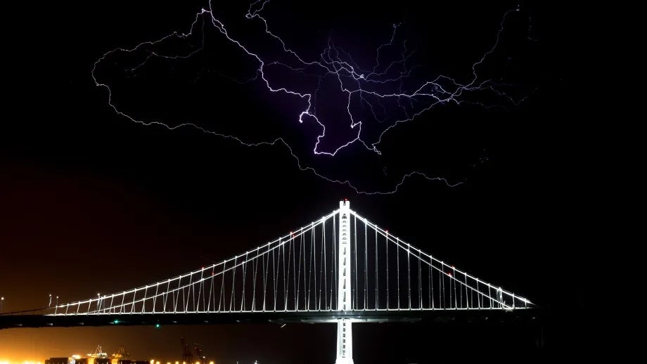 The San Francisco-Oakland Bay Bridge at night during a lightning storm.