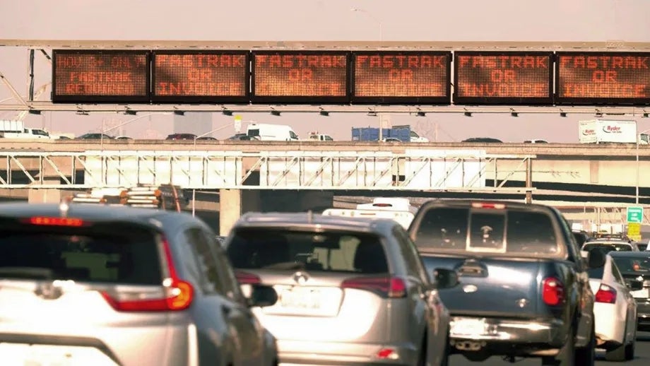 Heavy traffic beneath an electronic toll plaza sign indicating FasTrak or Invoice.