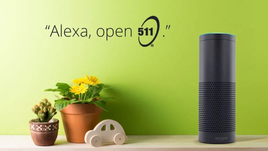 An Alexa unit sits on a shelf with a flower pot and a cactus in front of a green background with the words "Alexa, open 511" beside it.